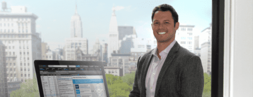 Man smiling with computer and city in background.