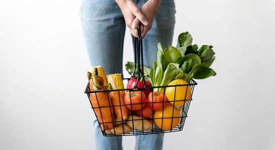 Person wearing jeans holding a basket of fruit.