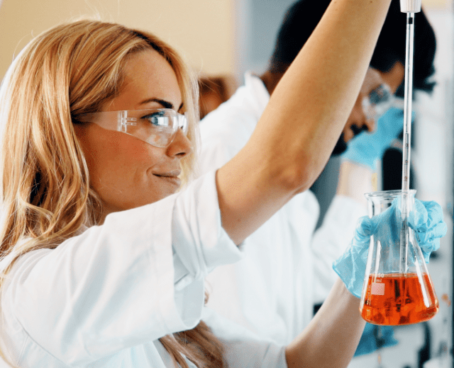 Female scientist looking at beaker in science lab.